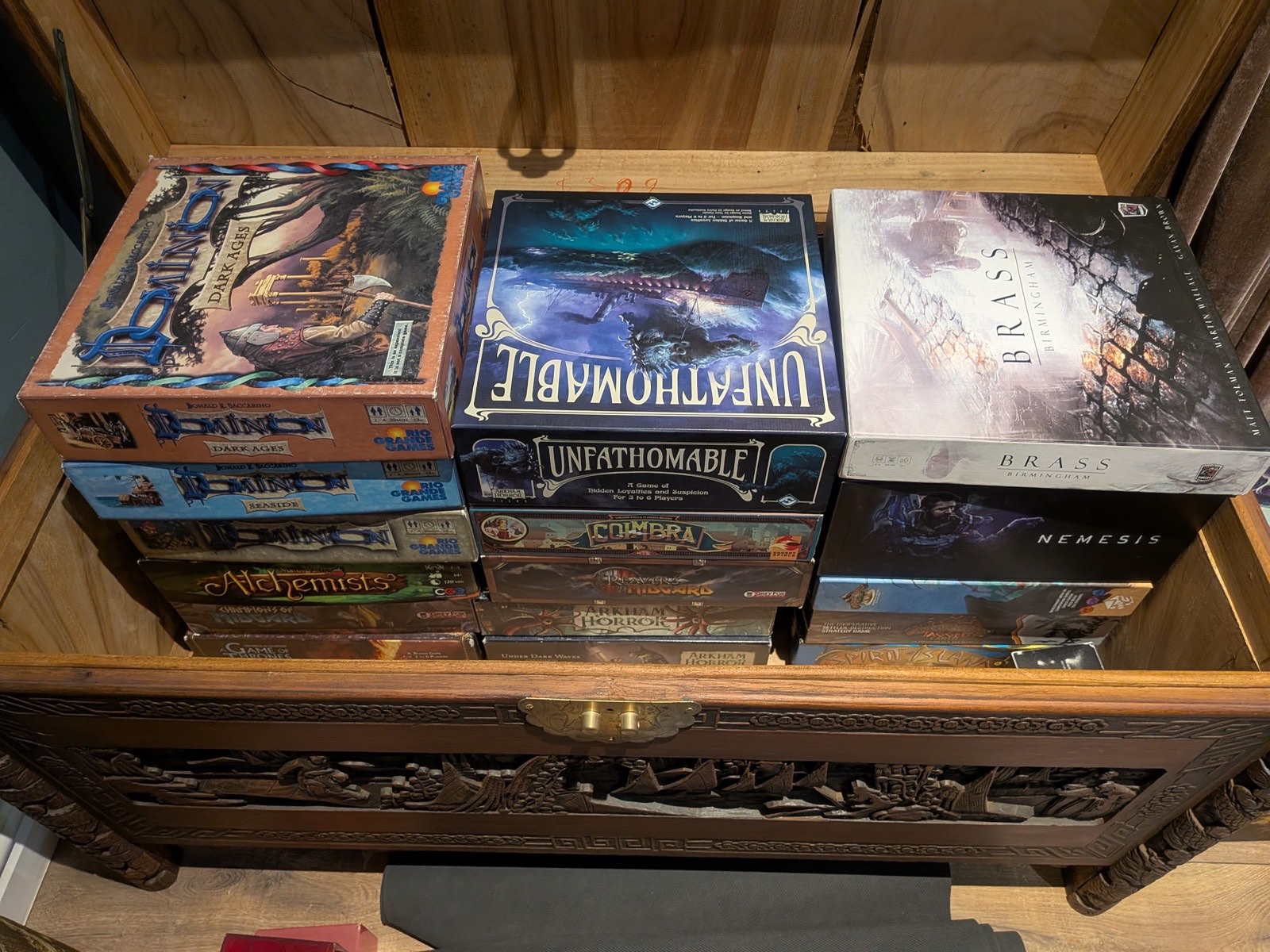 A carved chest full of board games: Unfathomable, Brass Birmingham, Dominion, Nemesis, Spirit Island