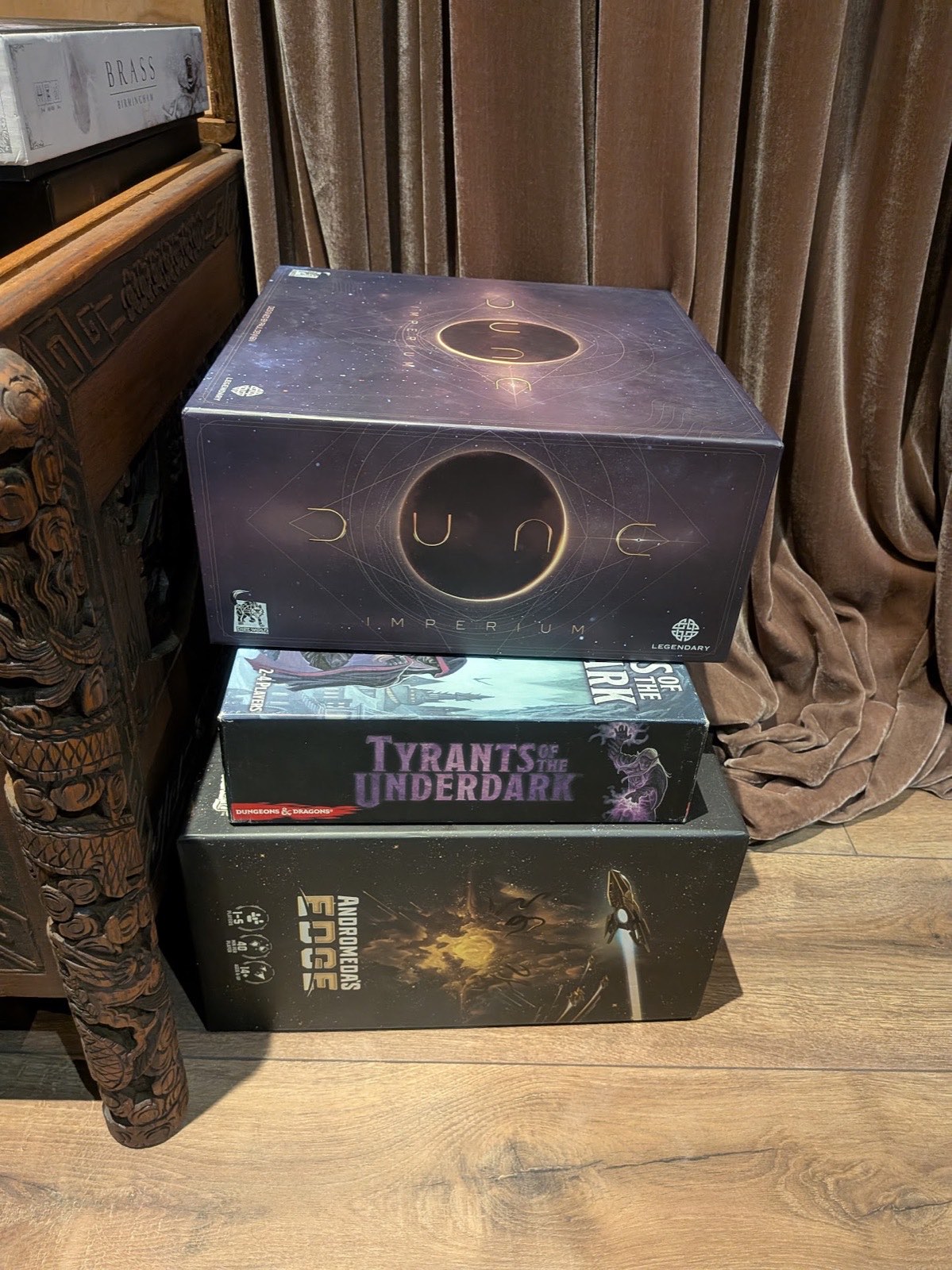 Dune Imperium, Tyrants of the Underdark and Andromeda's Edge stacked by a velvet curtain