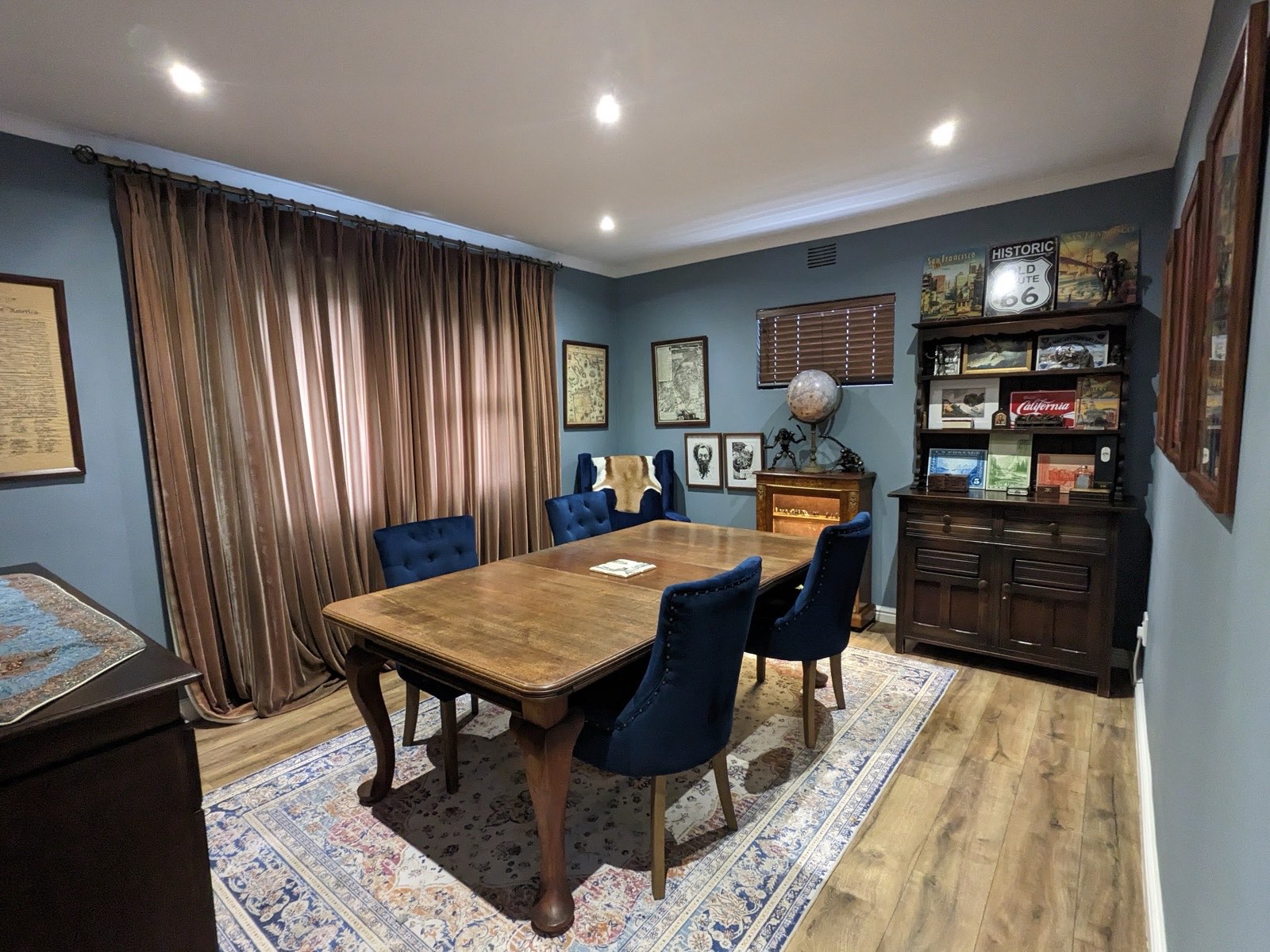 The parlour: a long walnut table with navy velvet chairs, brass curtains, maps and a globe